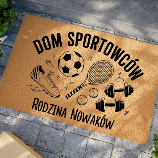Wycieraczka z napisem „Dom Sportowców” i personalizowanym nazwiskiem, ozdobiona motywami sportowymi.