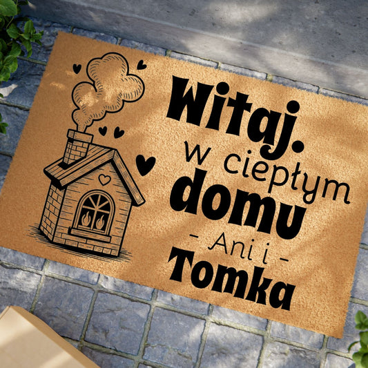Wycieraczka z napisem „Witaj w ciepłym domu” i personalizacją imion, ozdobiona motywem domku.
